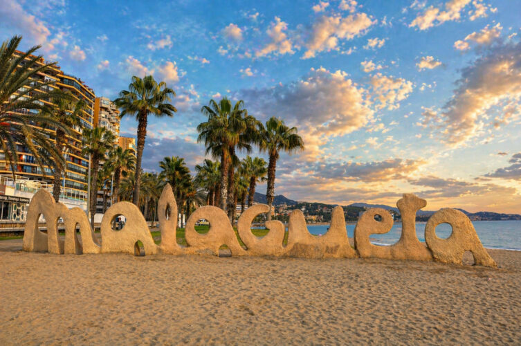 Napis Playa de La Malagueta na plaży w Malaga o zachodzie dnia – palmy i nadmorska promenada Costa del Sol
