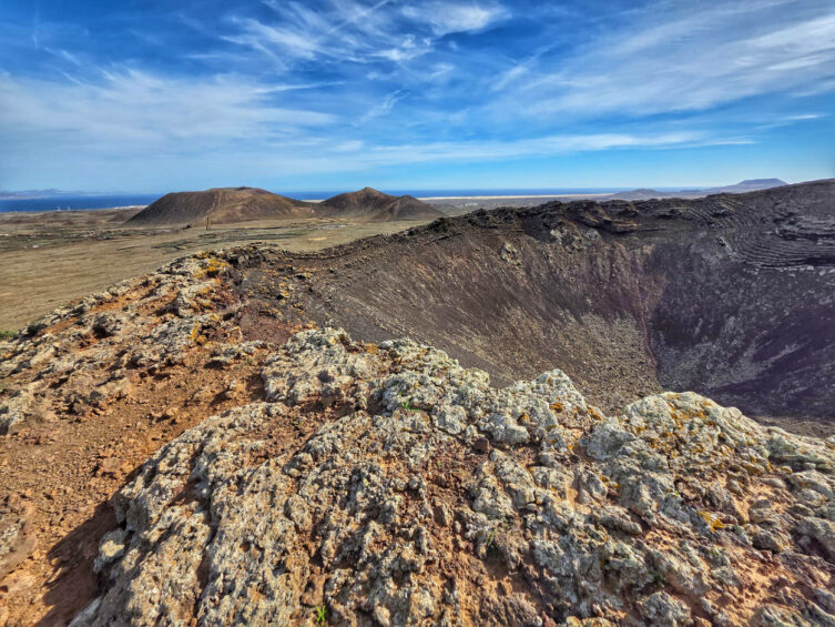 フエルテベントゥラ島のカルデロン・ホンド火山の火口からの眺め。背景には険しい火山地形と海が広がっている。